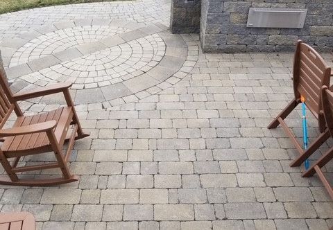 Paver patio with a circular design, two wooden chairs and stone wall.