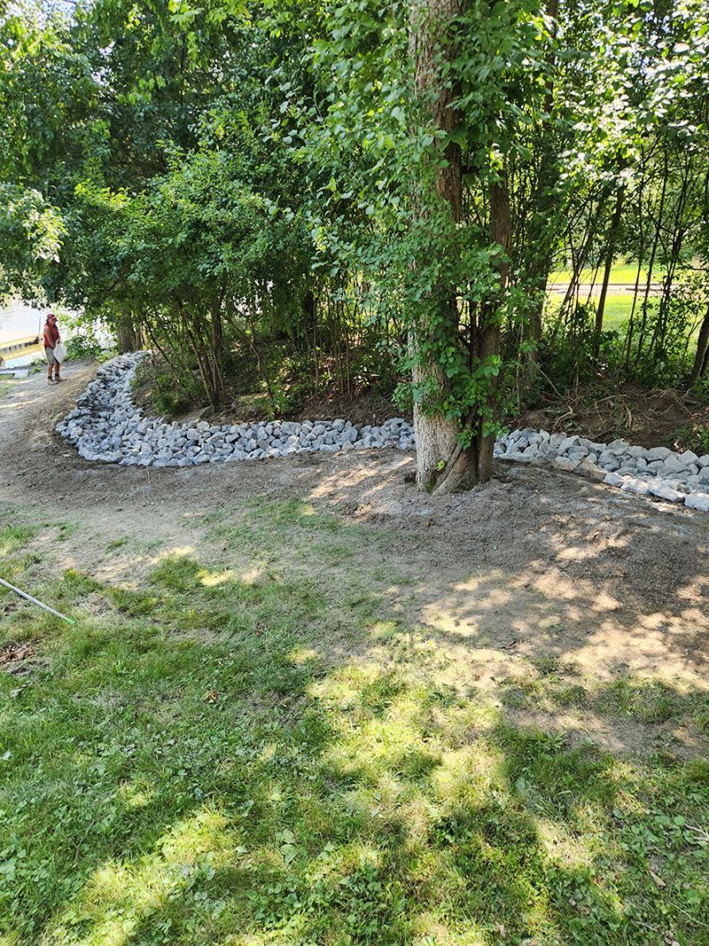 Rocks forming a retaining wall along a dirt path near trees and grass.