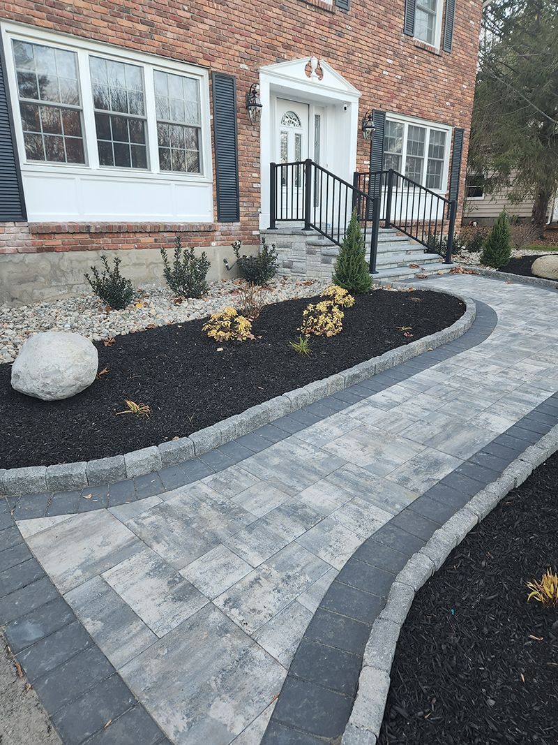Brick house with a paved walkway curving toward the entrance; a ramp and railing lead to the door.