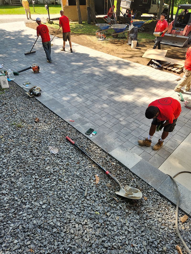 Construction workers in red shirts laying pavers on a stone pathway.