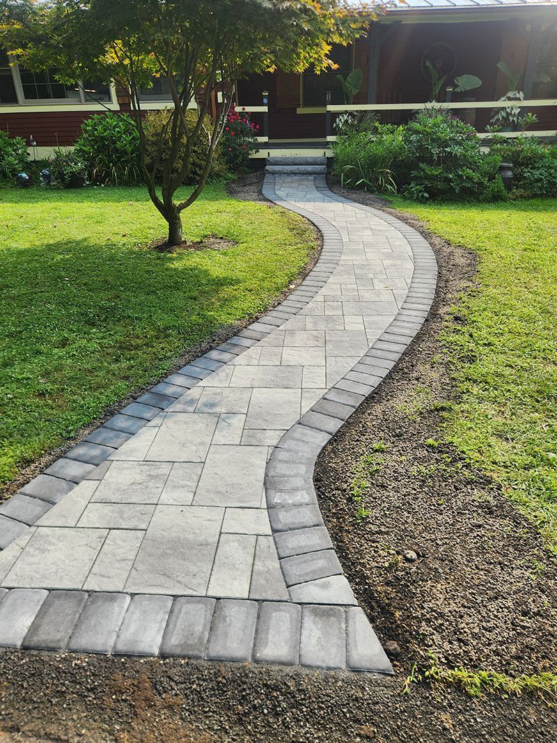 Stone walkway curves through a grassy lawn towards a house with a small tree.