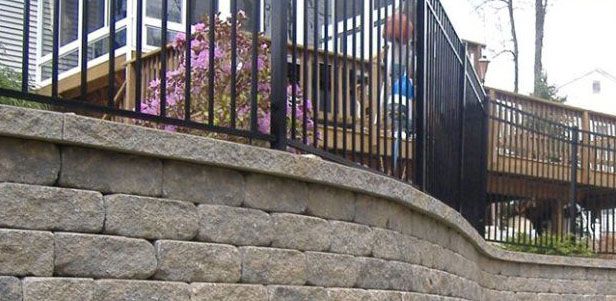 A retaining wall with a black metal fence and wooden deck in the background.