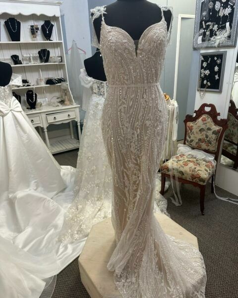 Beaded ivory bridal gown on a mannequin in a bridal shop with dresses and chairs nearby