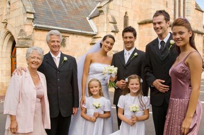 Wedding party posing outside a stone building, with bride, groom, children, and family members smiling.