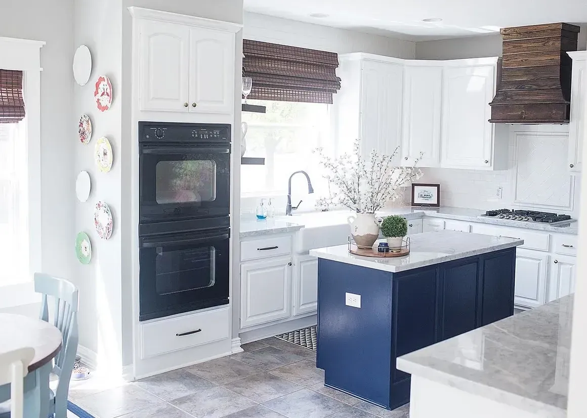A kitchen with white cabinets , a black oven , a sink , and a blue island.