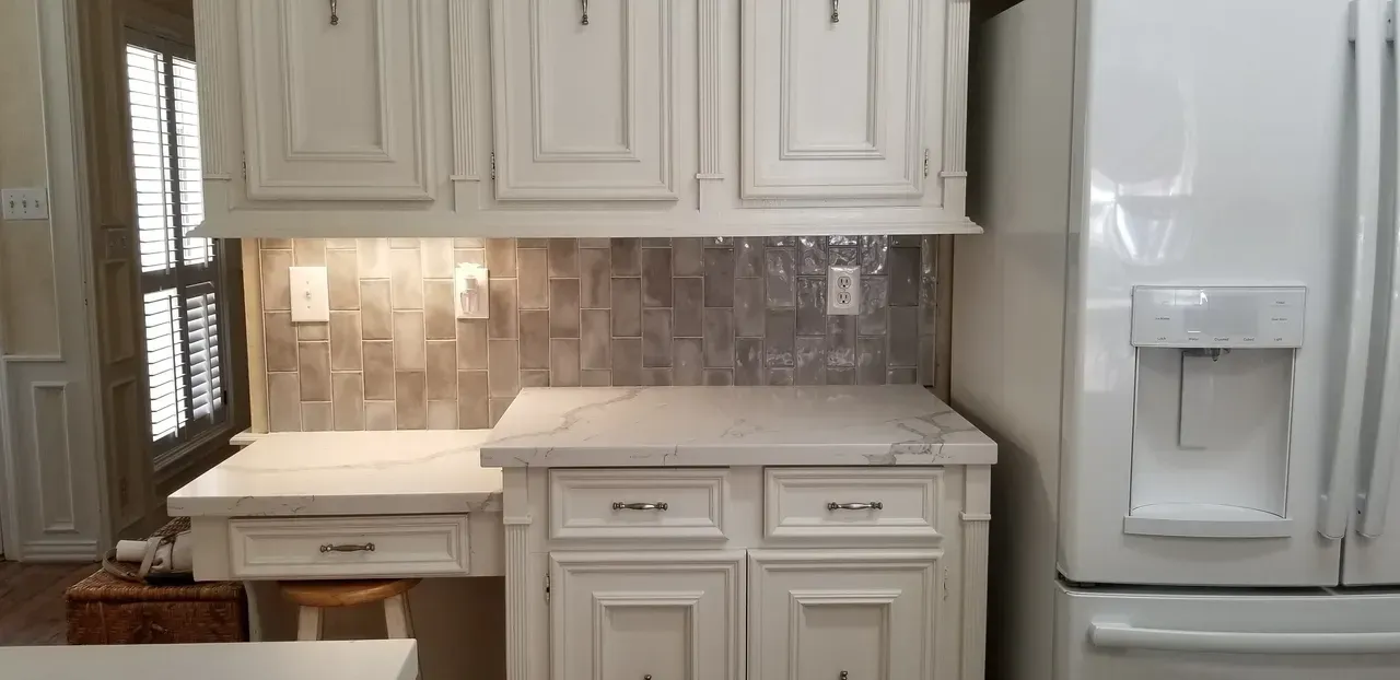 A kitchen with white cabinets , a refrigerator and a desk.