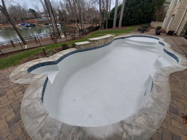 Empty empty swimming pool with a stone deck and raised spa in a backyard.
