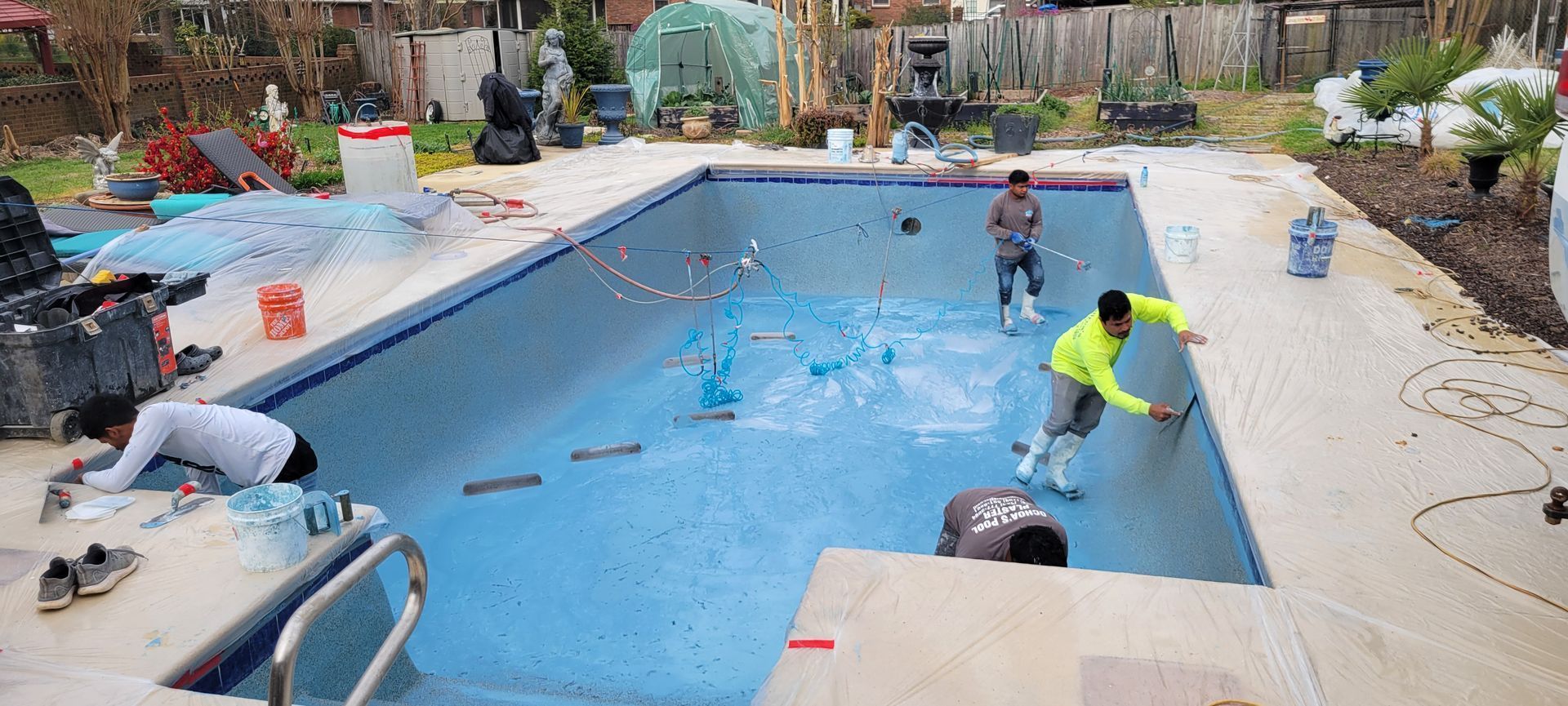 People working to paint a backyard swimming pool bright blue during renovation