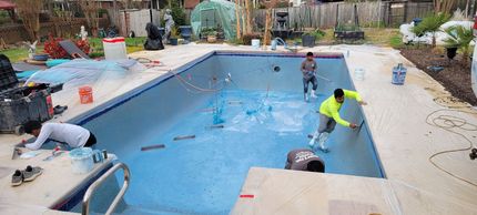 People working to paint a backyard swimming pool bright blue during renovation