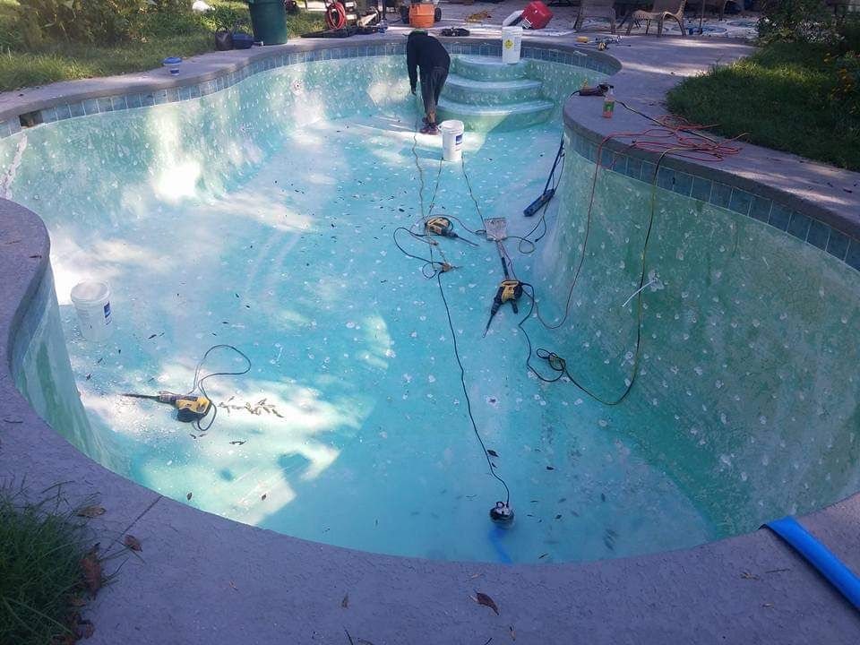 Empty swimming pool being cleaned, with hoses and equipment inside and a person at the far end