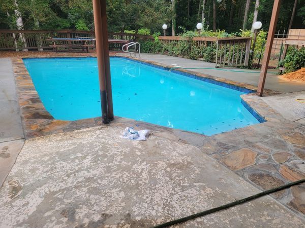 Outdoor swimming pool with blue water, stone deck, and surrounding greenery under a covered area