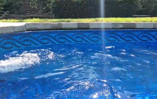 Blue swimming pool with rippling water and a patterned tile border in sunlight
