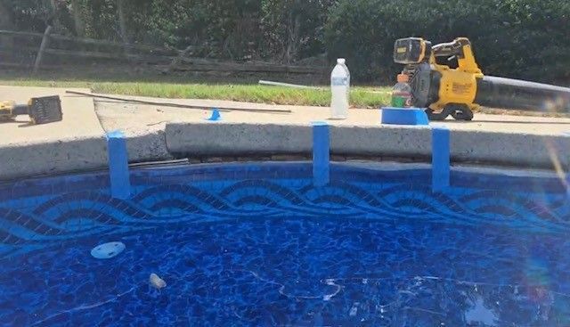 Blue pool water with a yellow pool cleaner and a white bottle on the deck edge