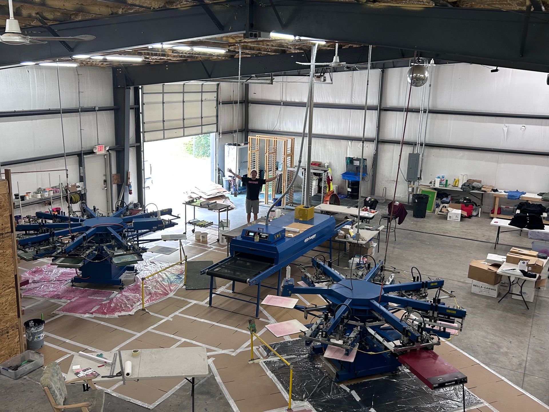 Large warehouse with multiple screen printing machines and a person standing near a conveyor dryer.