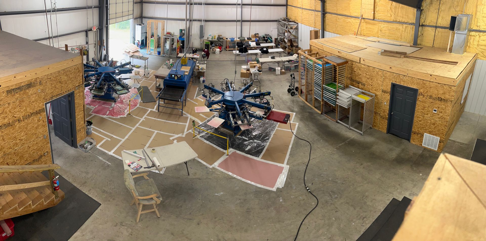 Large workshop with printing equipment, makeshift cubicles, and various materials.