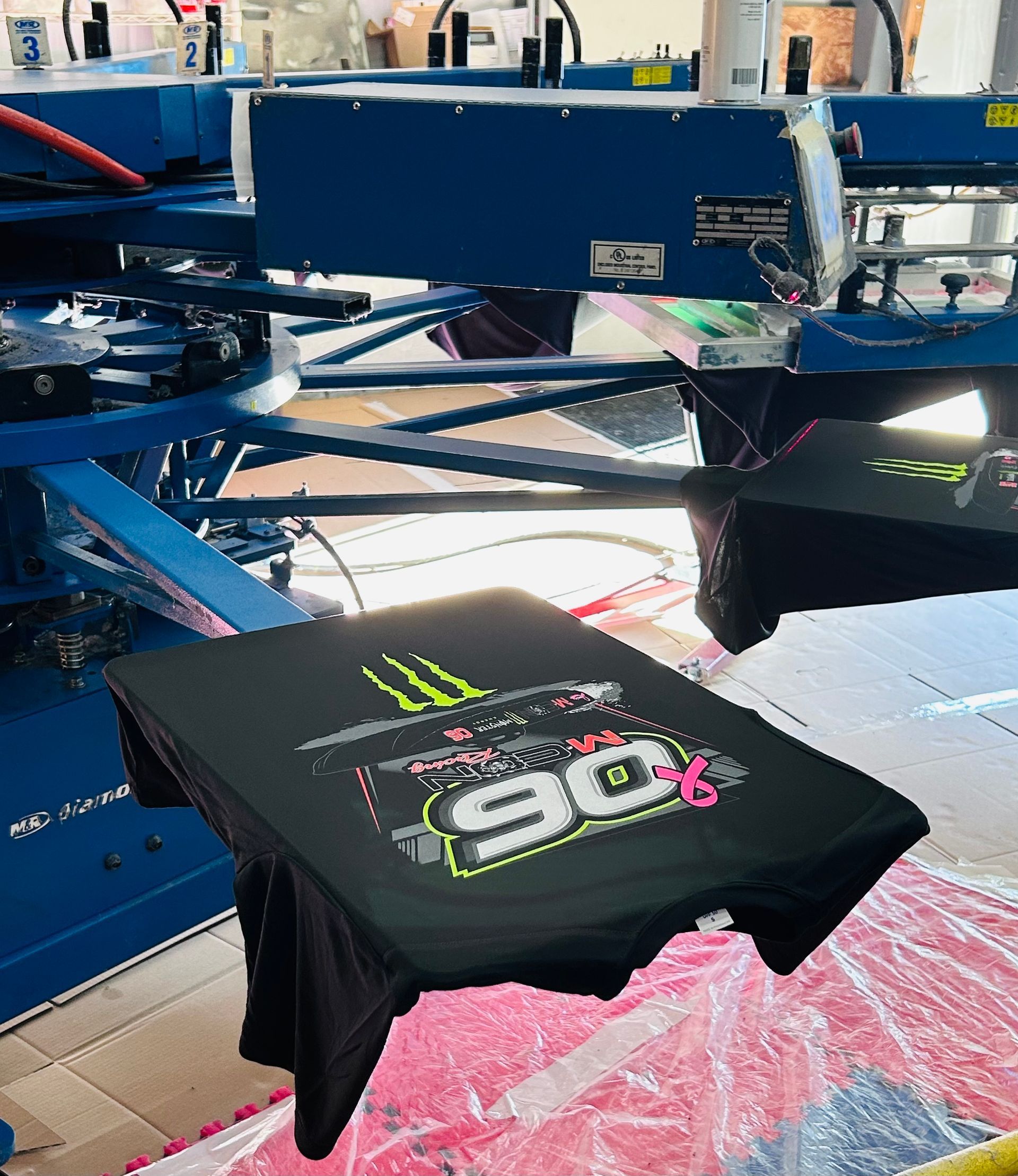 Black t-shirt with neon graphic on a screen printing machine, inside a factory.