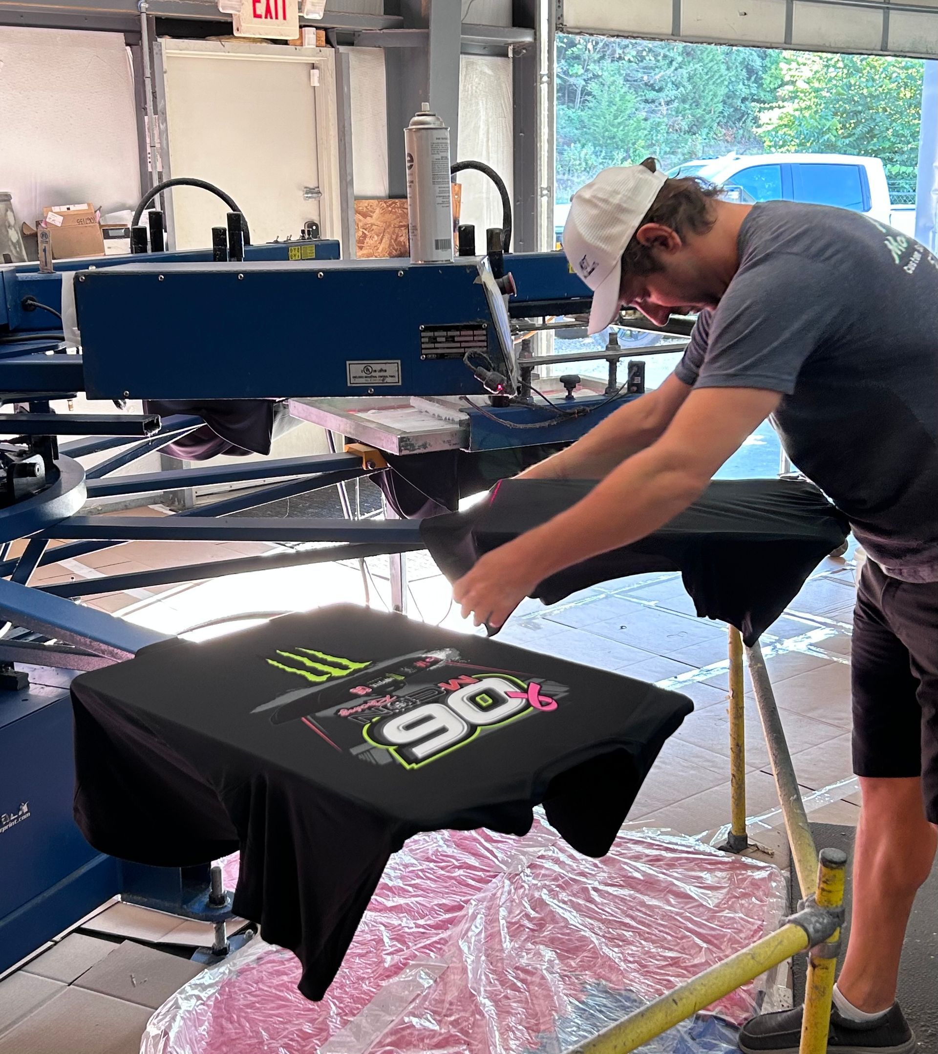 Man screen printing a black t-shirt with a colorful design in a workshop.
