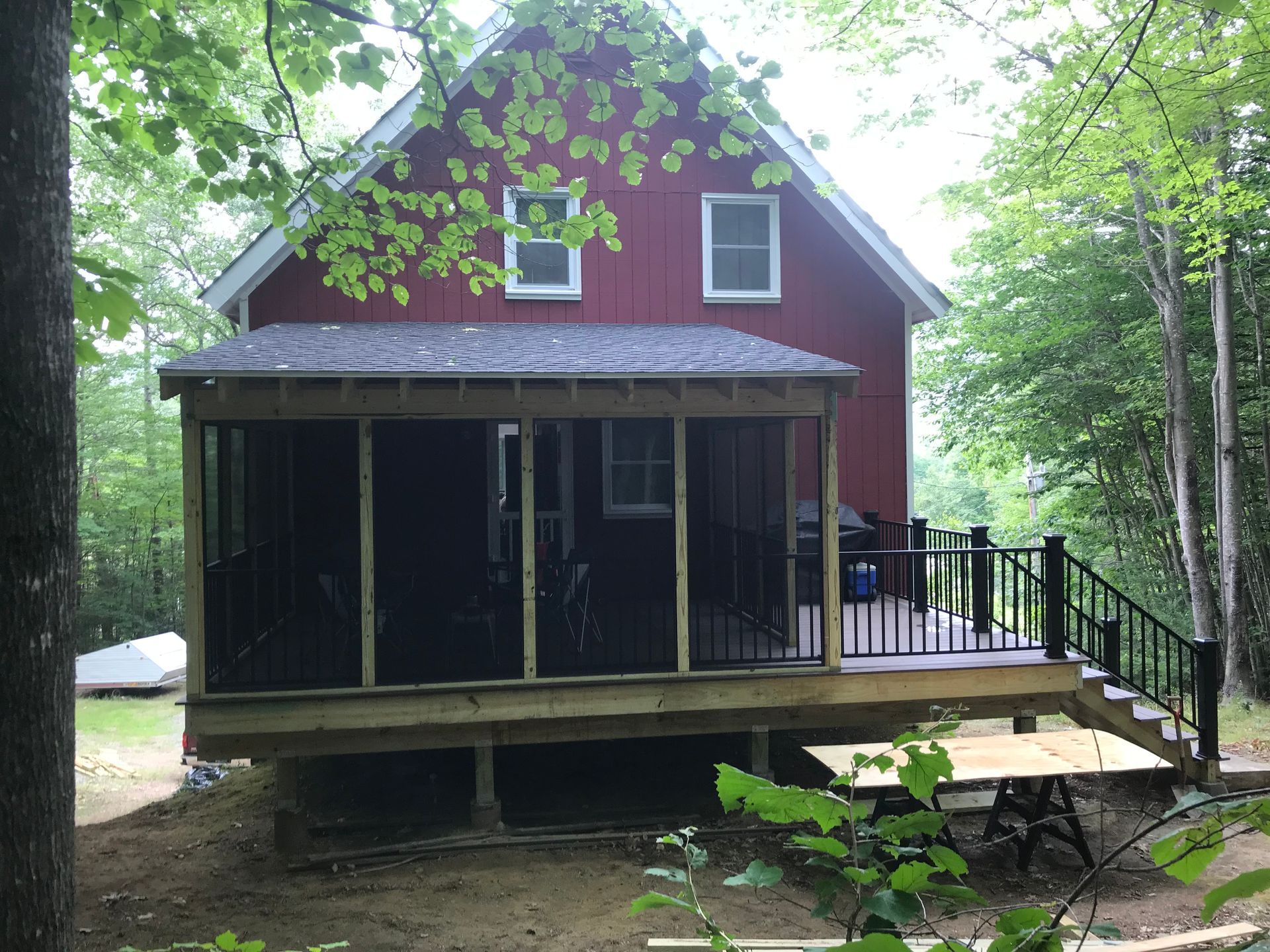 Red house with a screened porch and wooden deck in a wooded area.