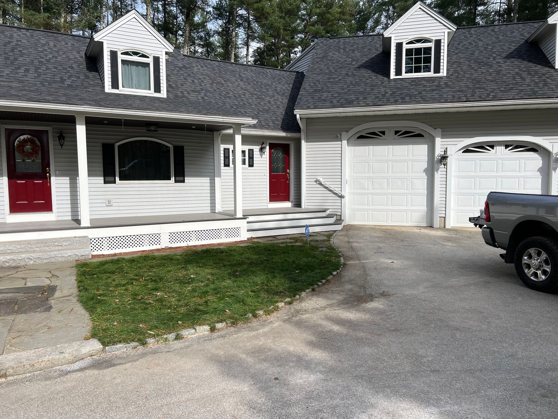 A gray house with a covered porch, red doors, and a two-car garage. A truck is parked in the driveway.