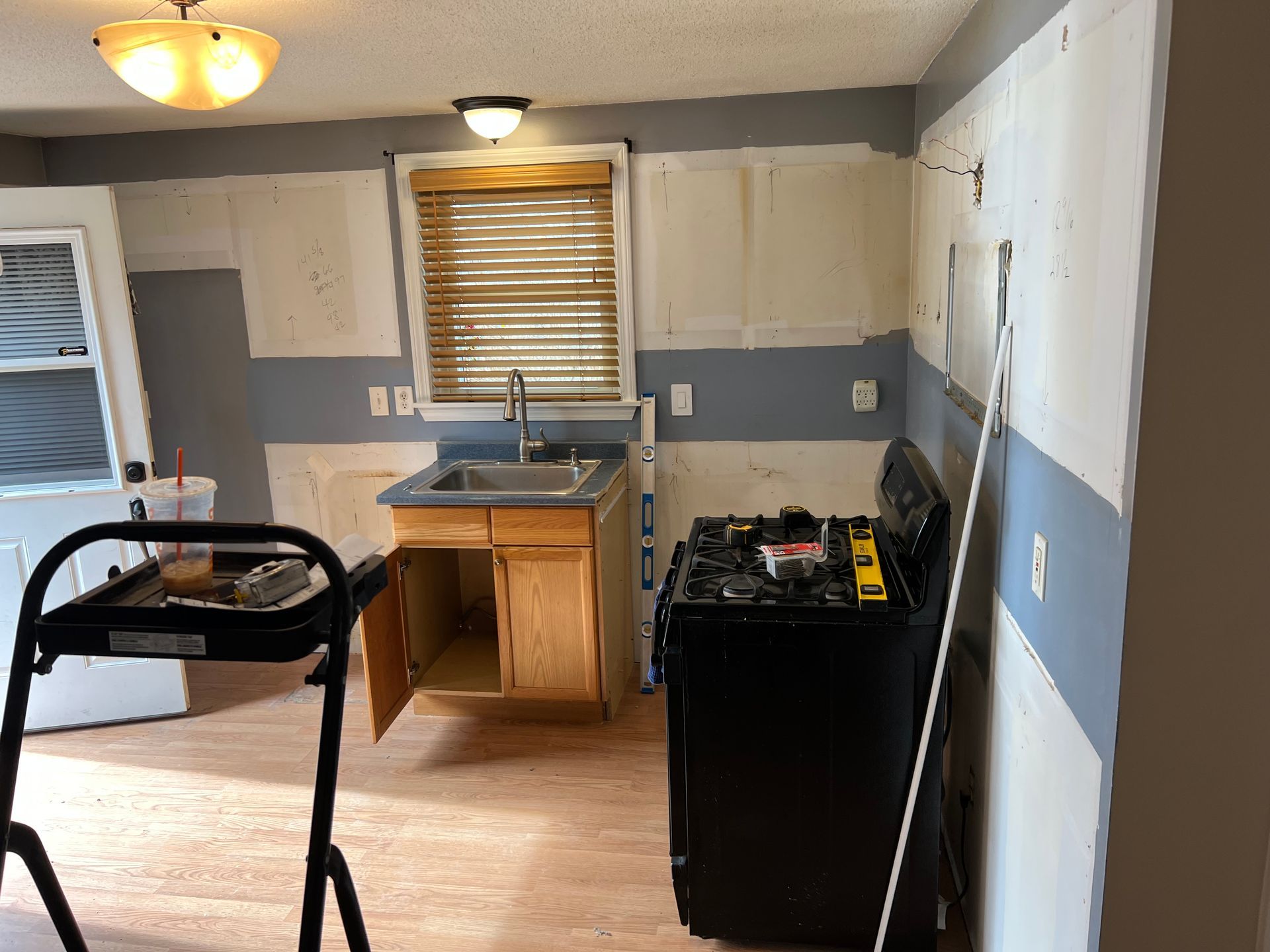 Kitchen remodel in progress: partially painted walls, sink, stove, open cabinet, step stool.