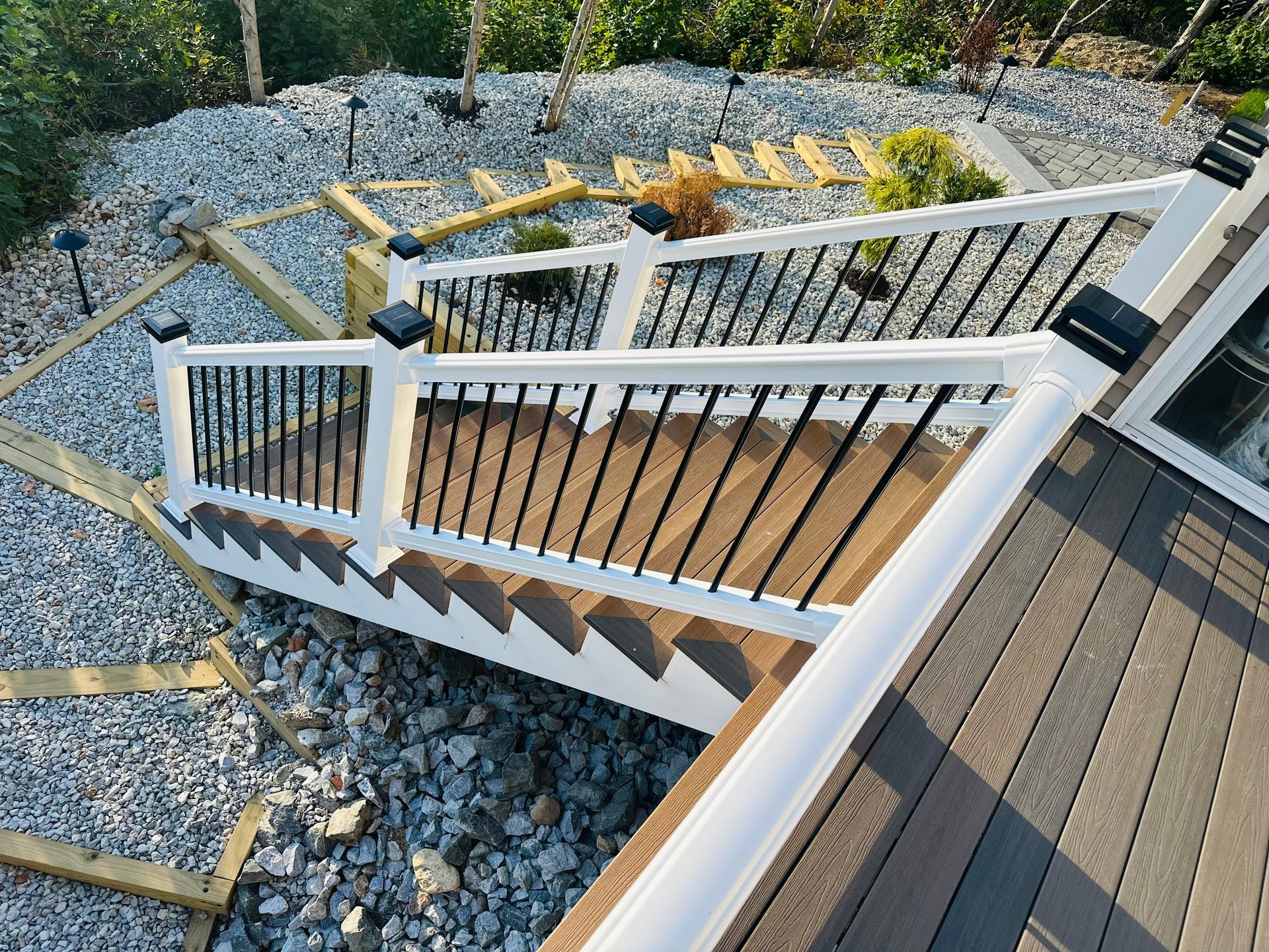 White deck stairs with black railing descend into a gravel yard.