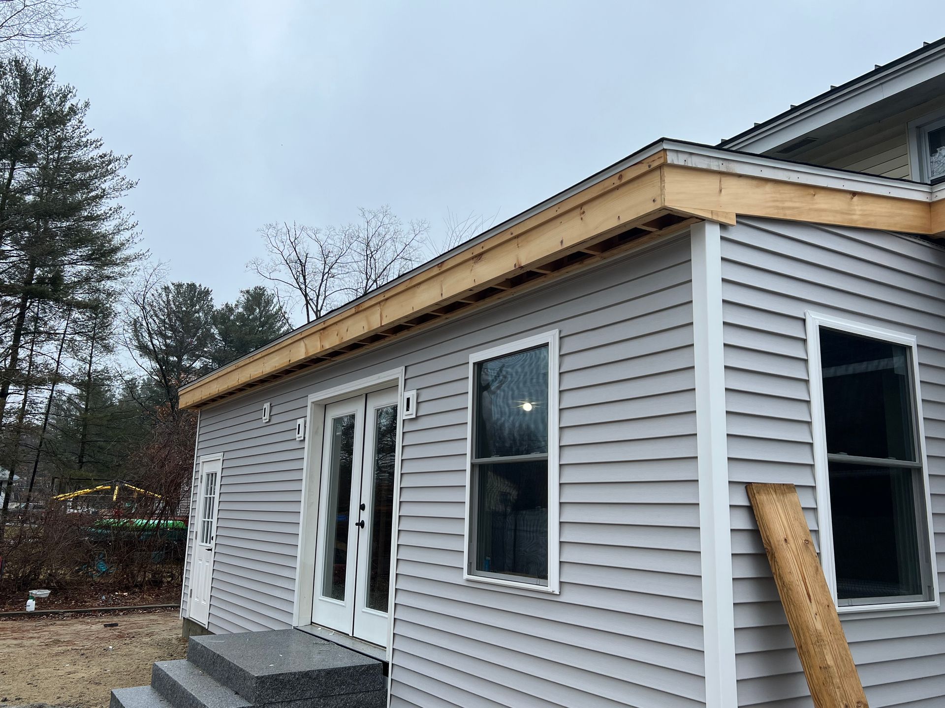 A home addition under construction with gray siding, windows, doors, and exposed wood framing.