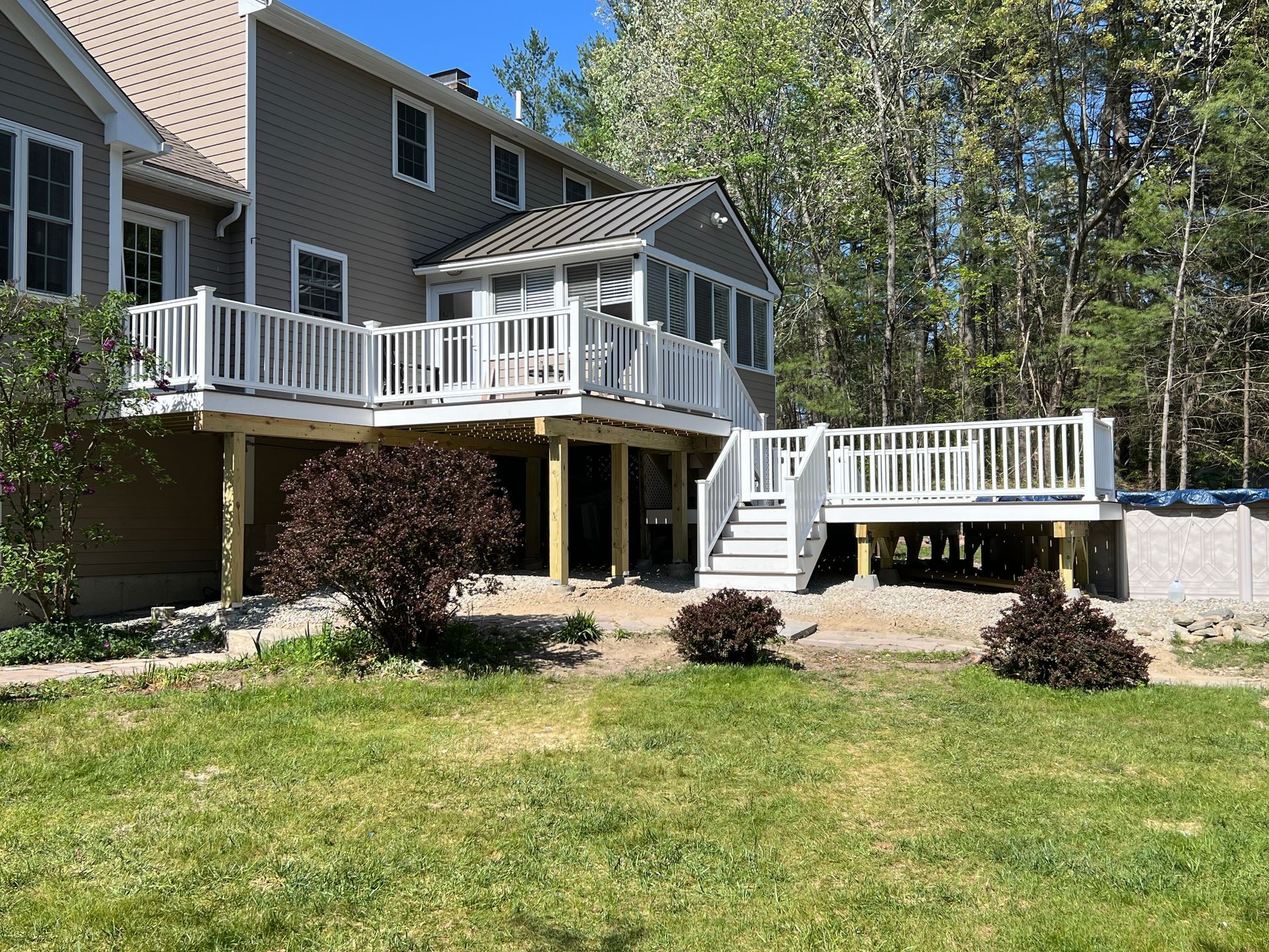 Back of a house with a multi-level wooden deck, white railings, and a screened porch.