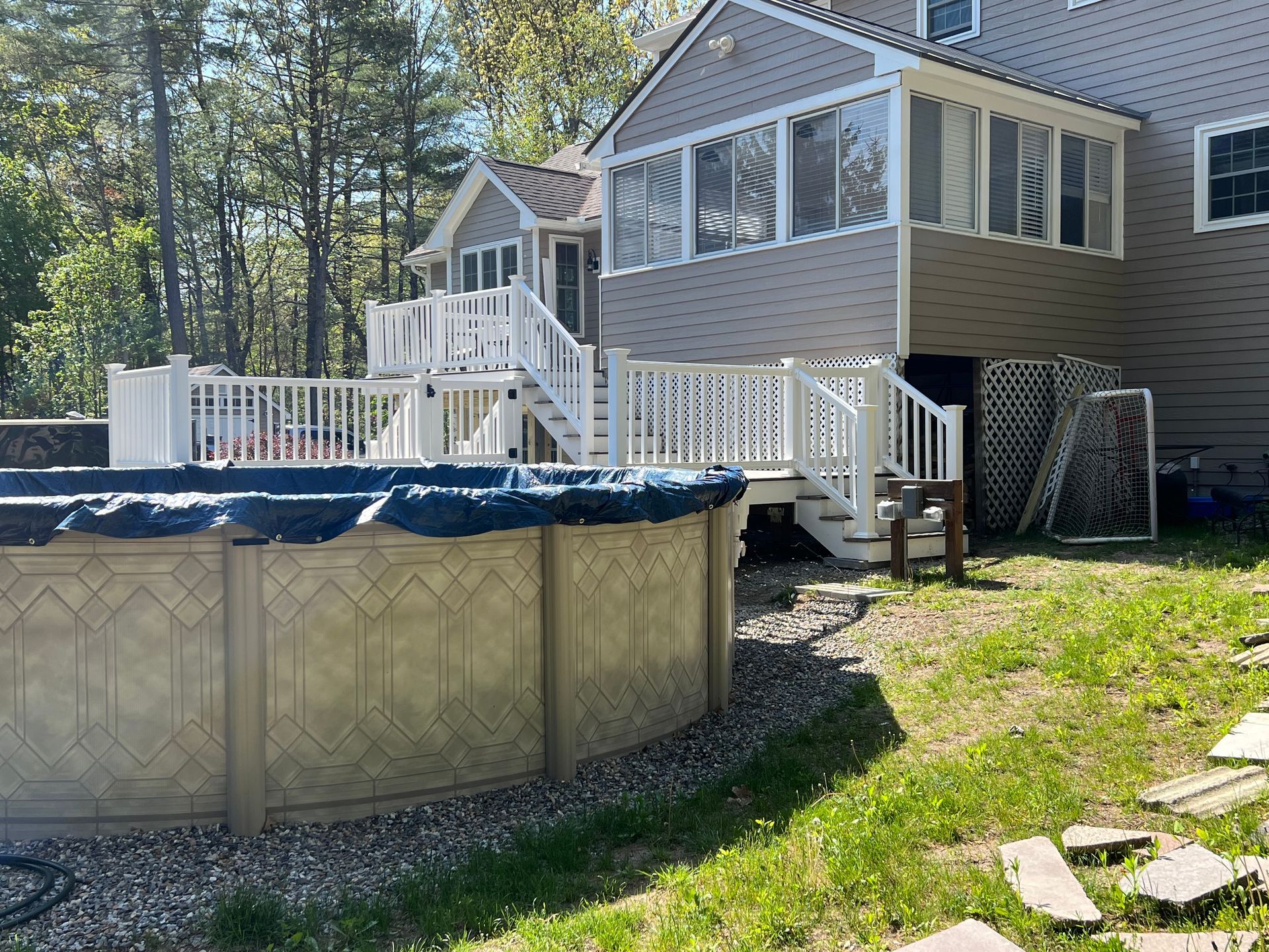 Above-ground pool next to a house with a deck and screened porch. Blue tarp covers the pool.