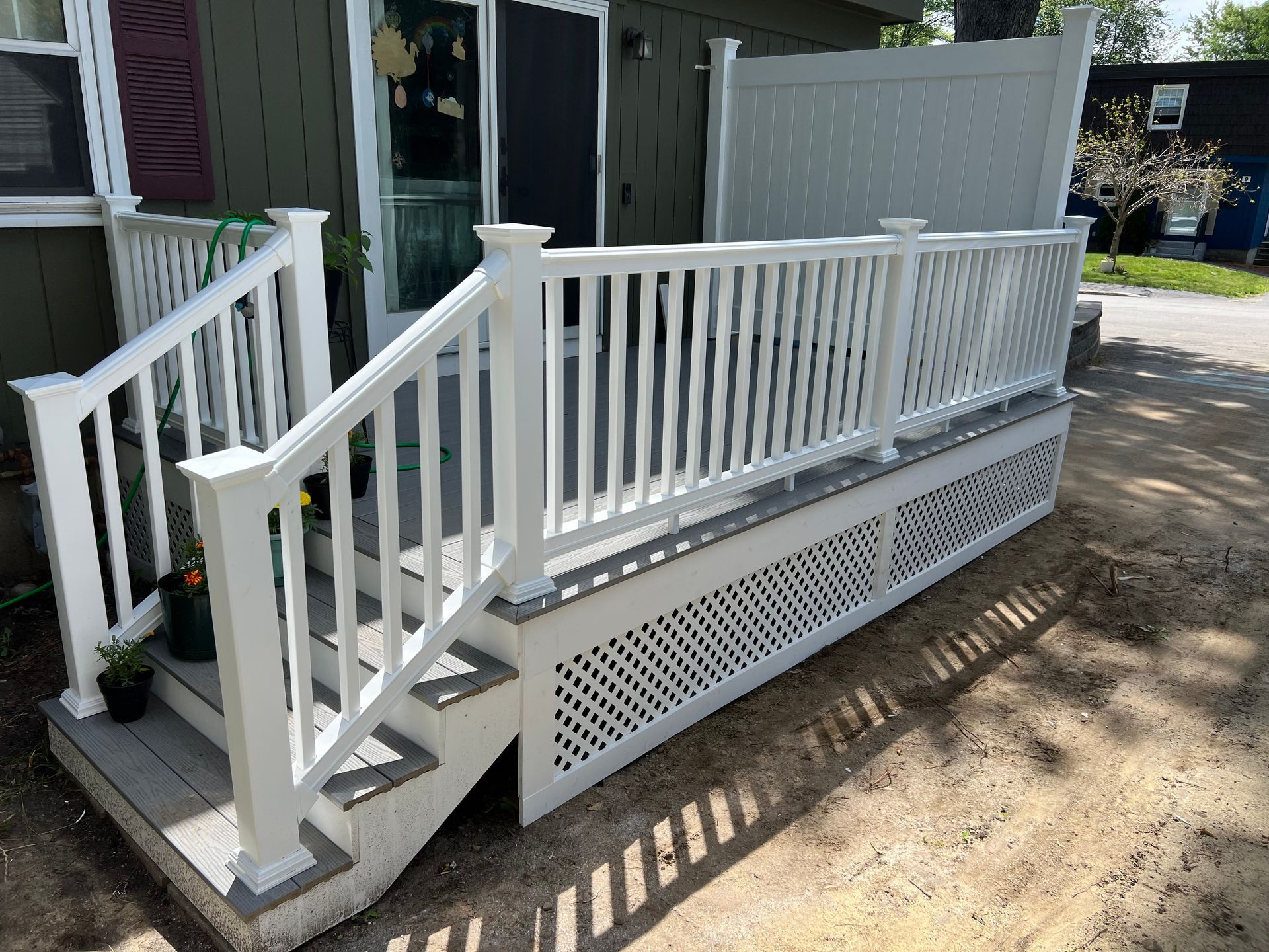 White deck with railing and stairs, attached to a green house.