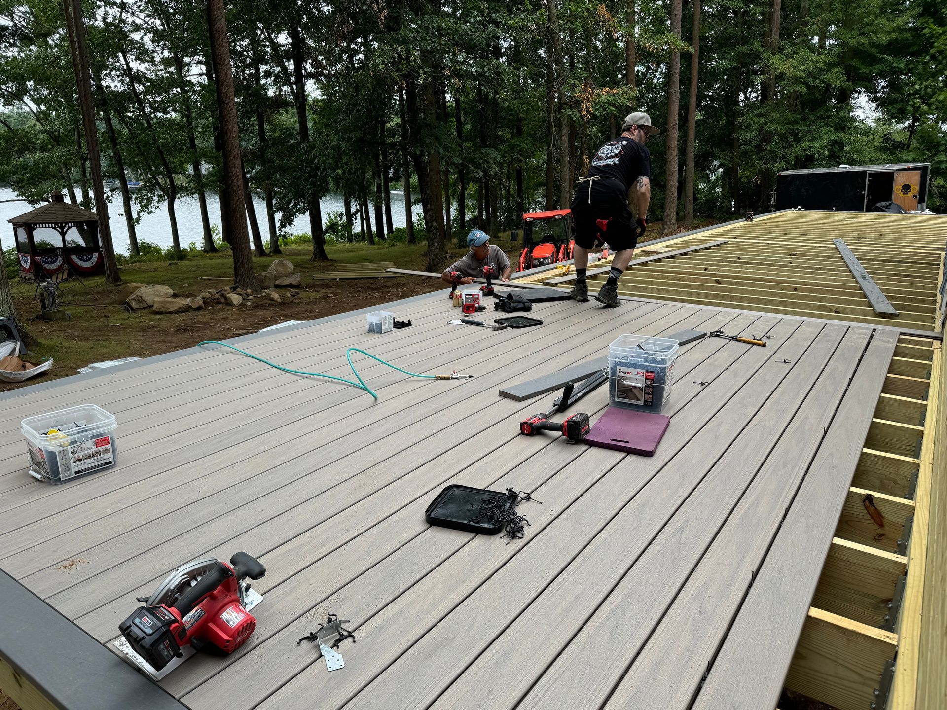 Two people building a composite deck outdoors, tools and materials scattered.