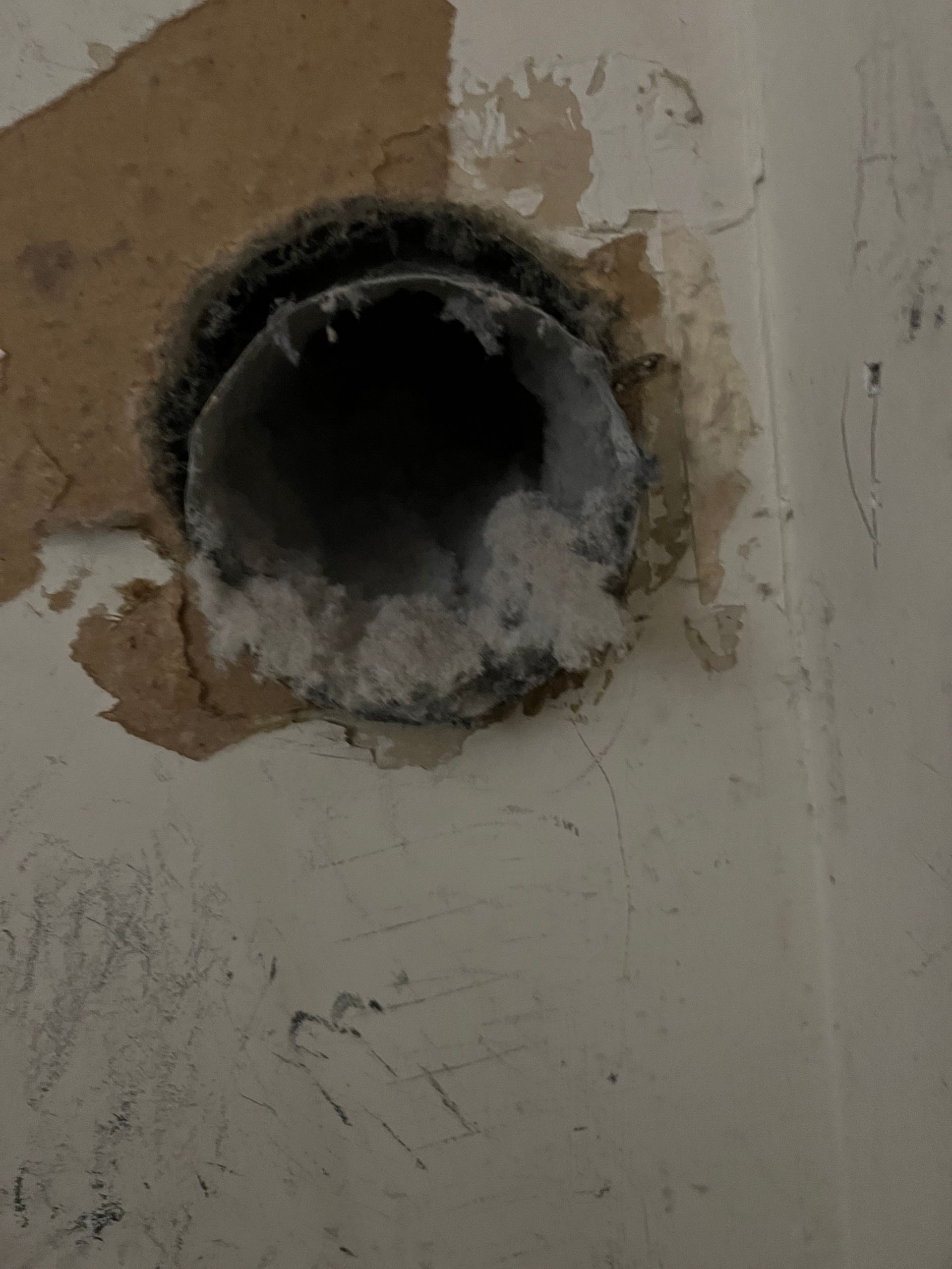Dryer vent opening in a wall, blocked by built-up lint.