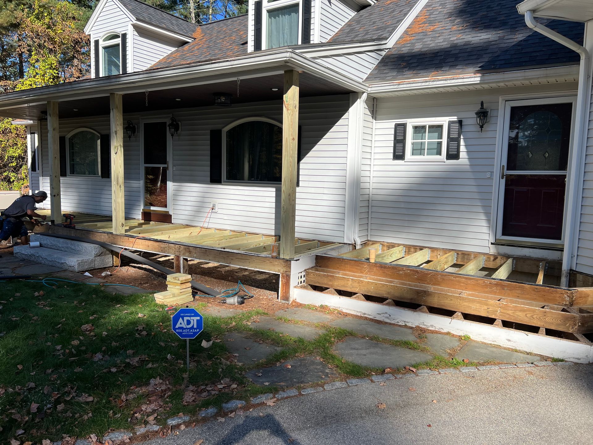 House with porch under renovation; new wood deck being built; white siding, gray roof.