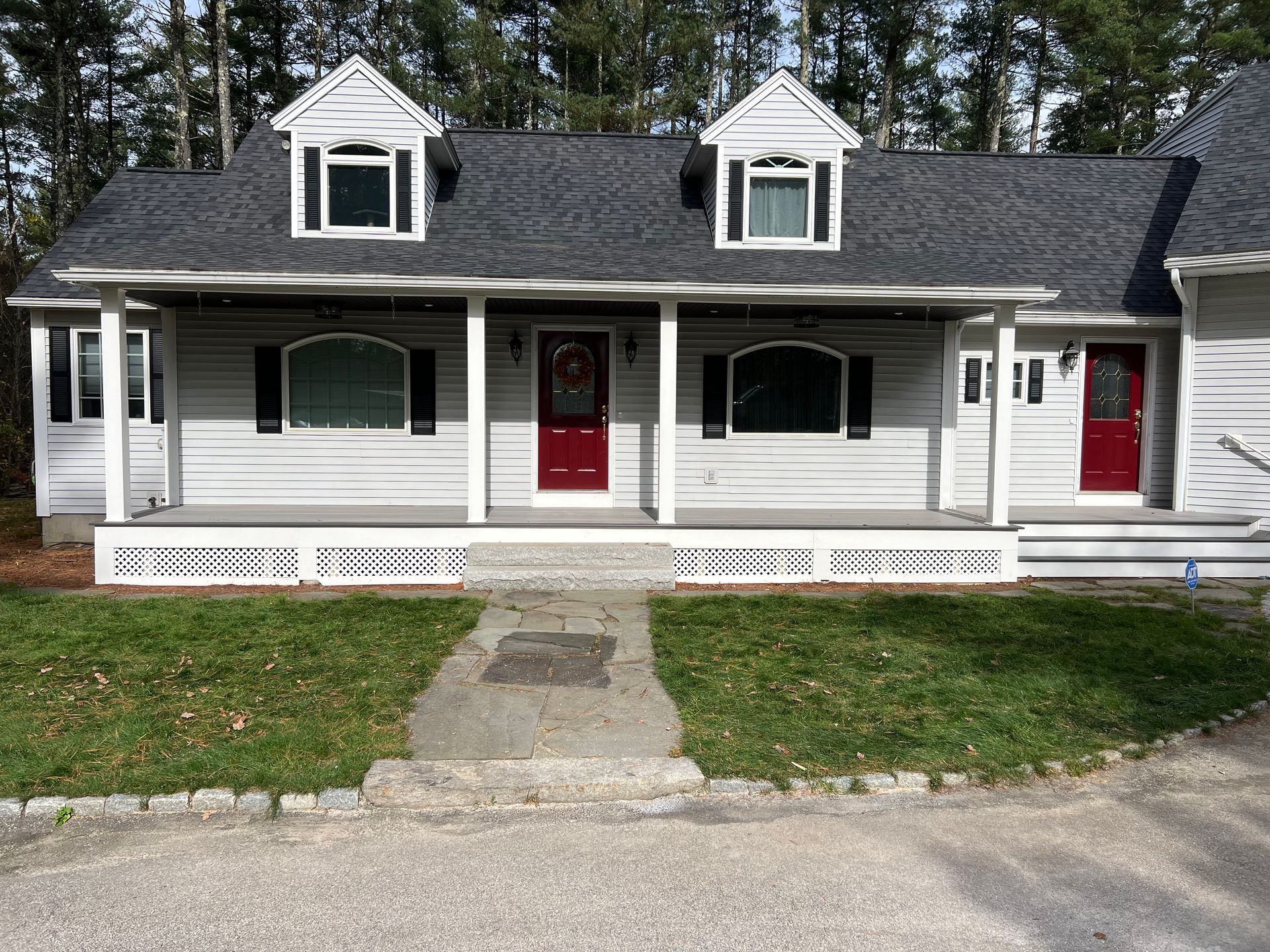 Gray house with red doors, white trim, a porch, and two dormers with black shutters.