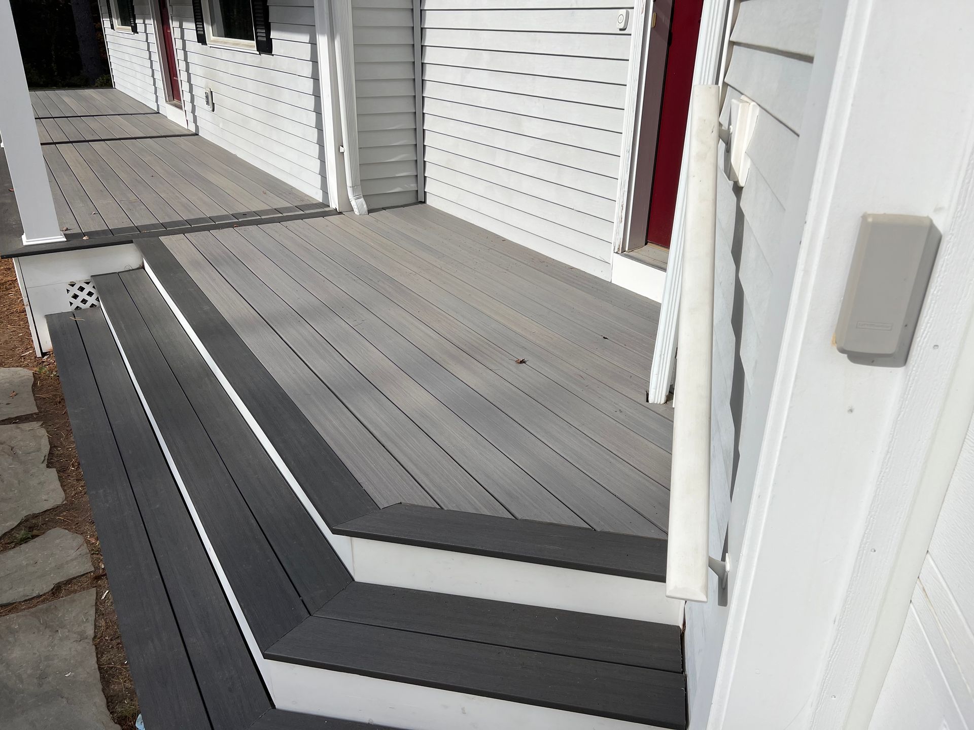 Gray composite deck with dark gray steps leading to a white house entrance.