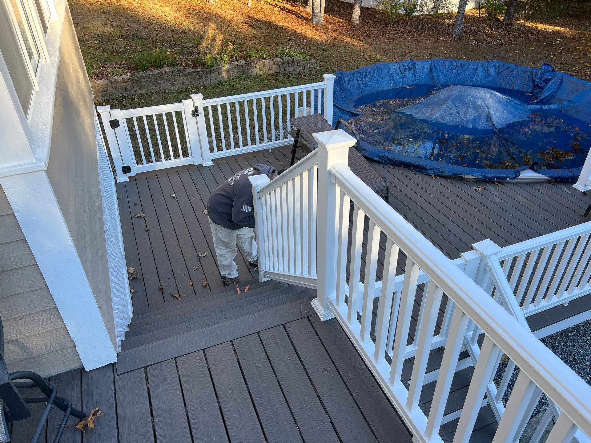 Person working on a wooden deck with white railings, near a covered pool.