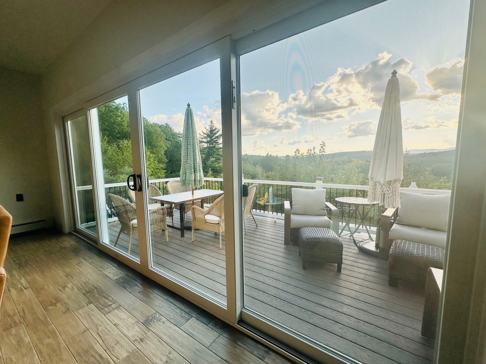 Wooden deck with patio furniture, large sliding glass doors, and a scenic outdoor view with a cloudy sky.