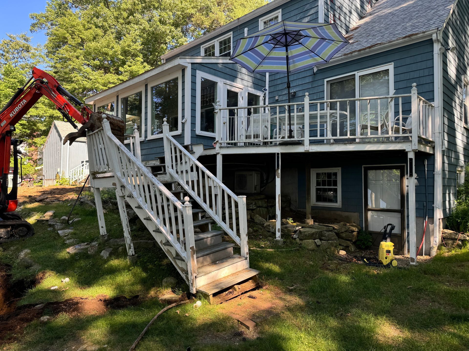 Blue house with white deck, stairs. Excavator in yard.