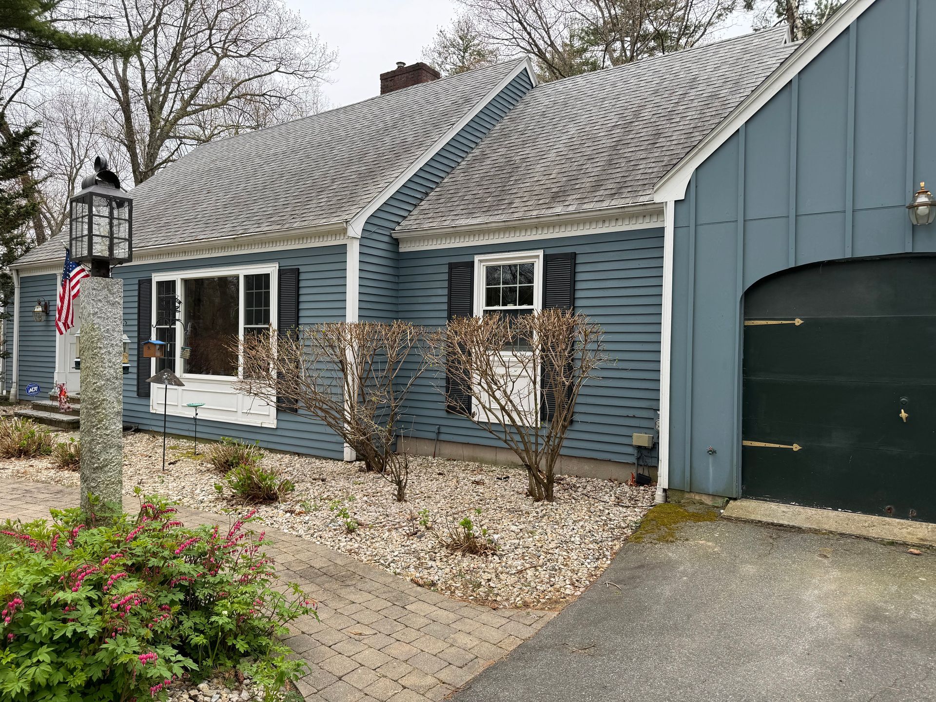 Blue house with a gray roof, driveway, and small bushes in front.