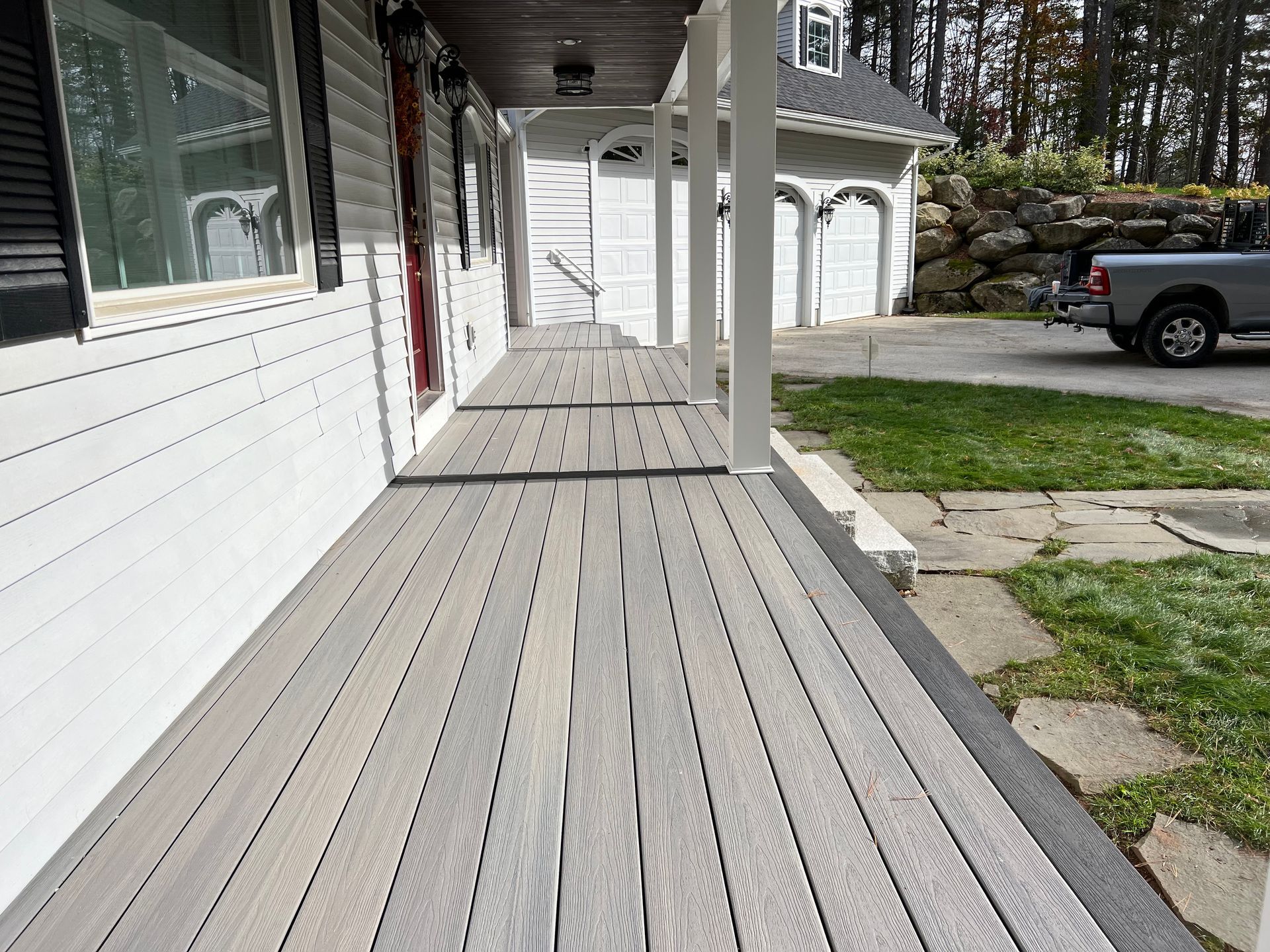 Long gray composite deck on a house with white pillars. Garage and truck in the background.