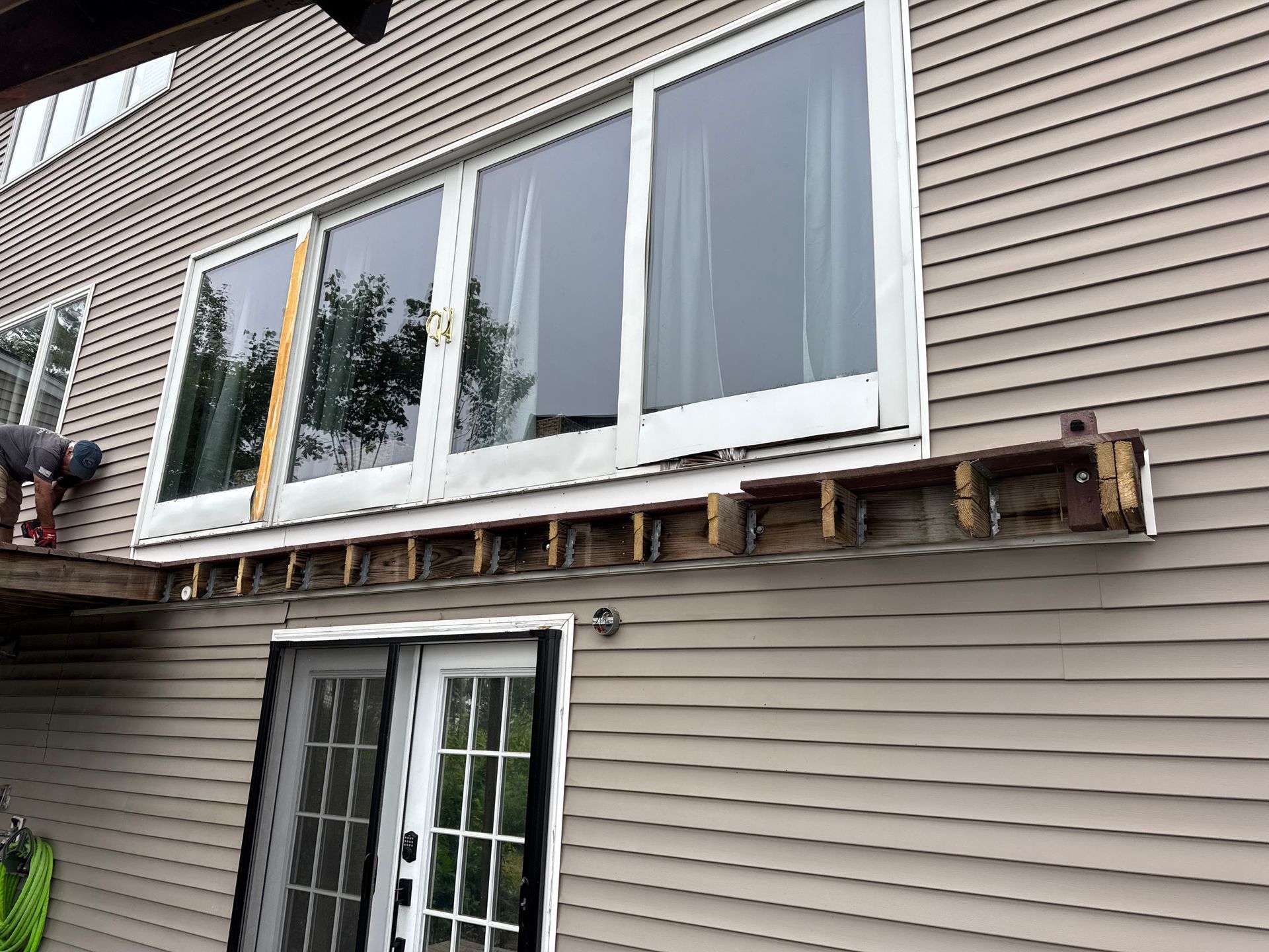 Exterior view: Damaged window frame above a sliding door, brown siding, construction in progress.