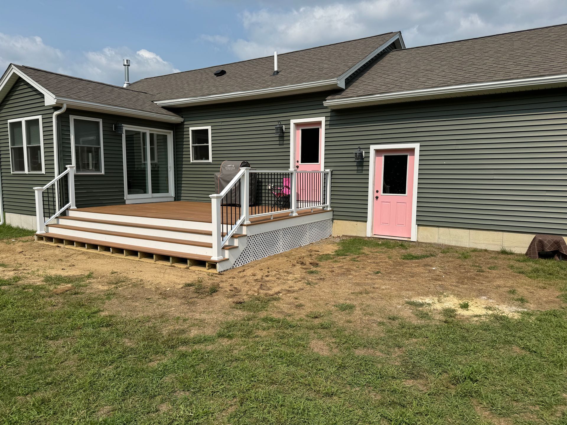 Backyard with gray siding, pink doors, a deck, and a grassy lawn.