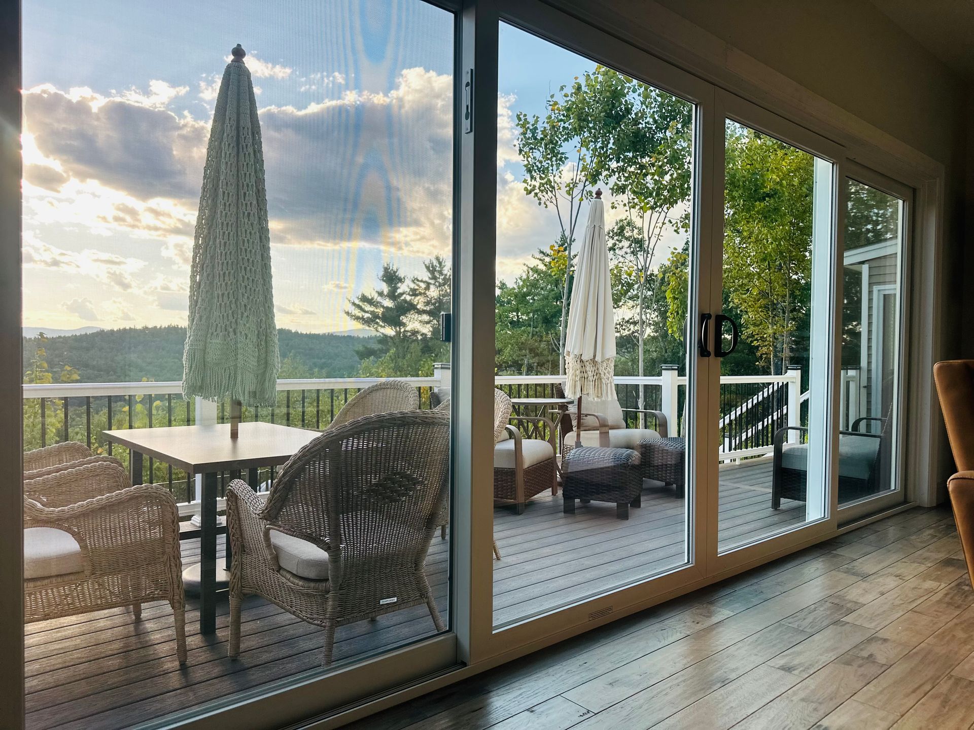 Patio with wicker furniture, umbrellas, and a view of a tree-covered hillside through sliding glass doors.