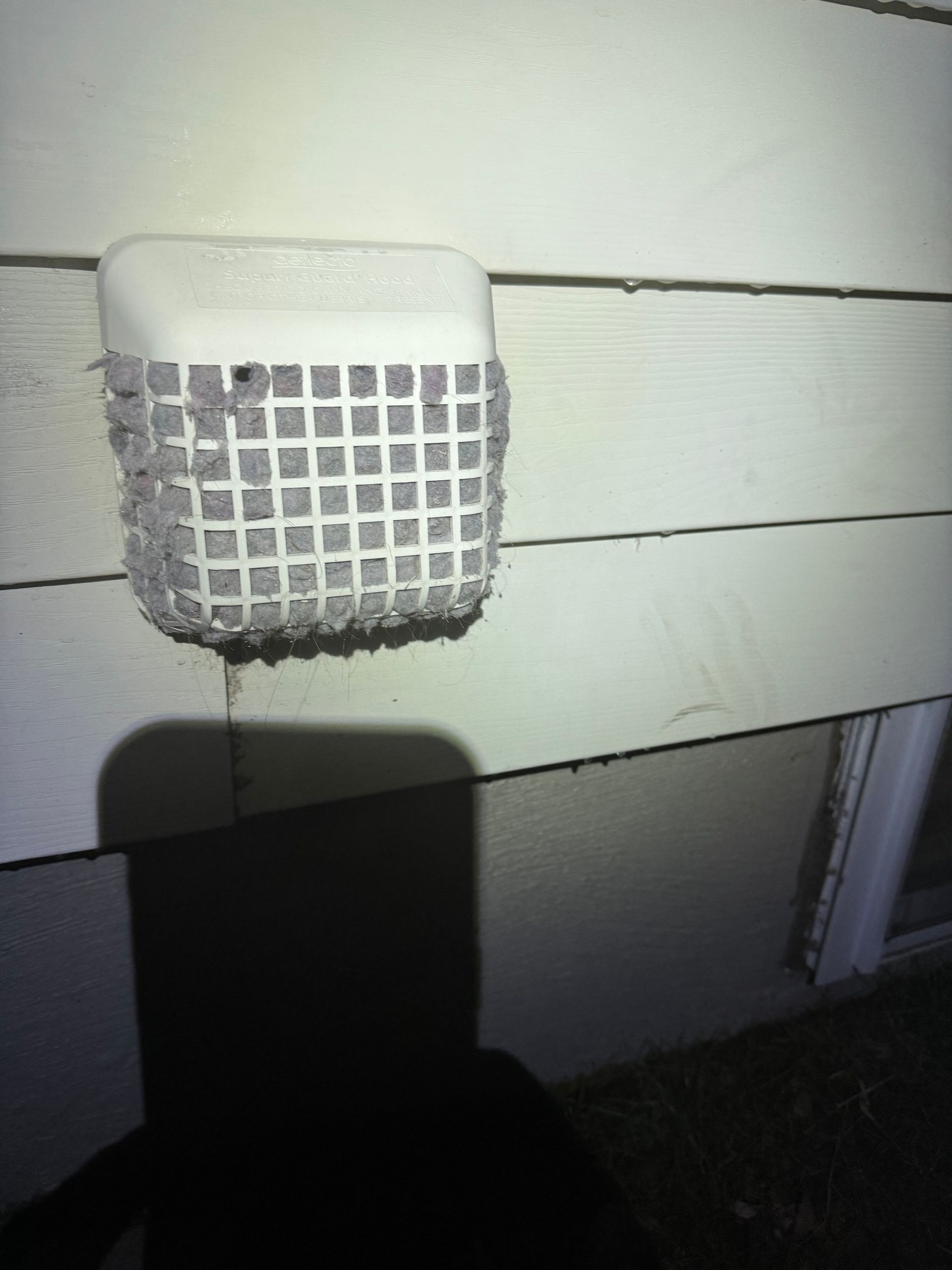 White dryer vent covered in lint on a cream-colored siding.