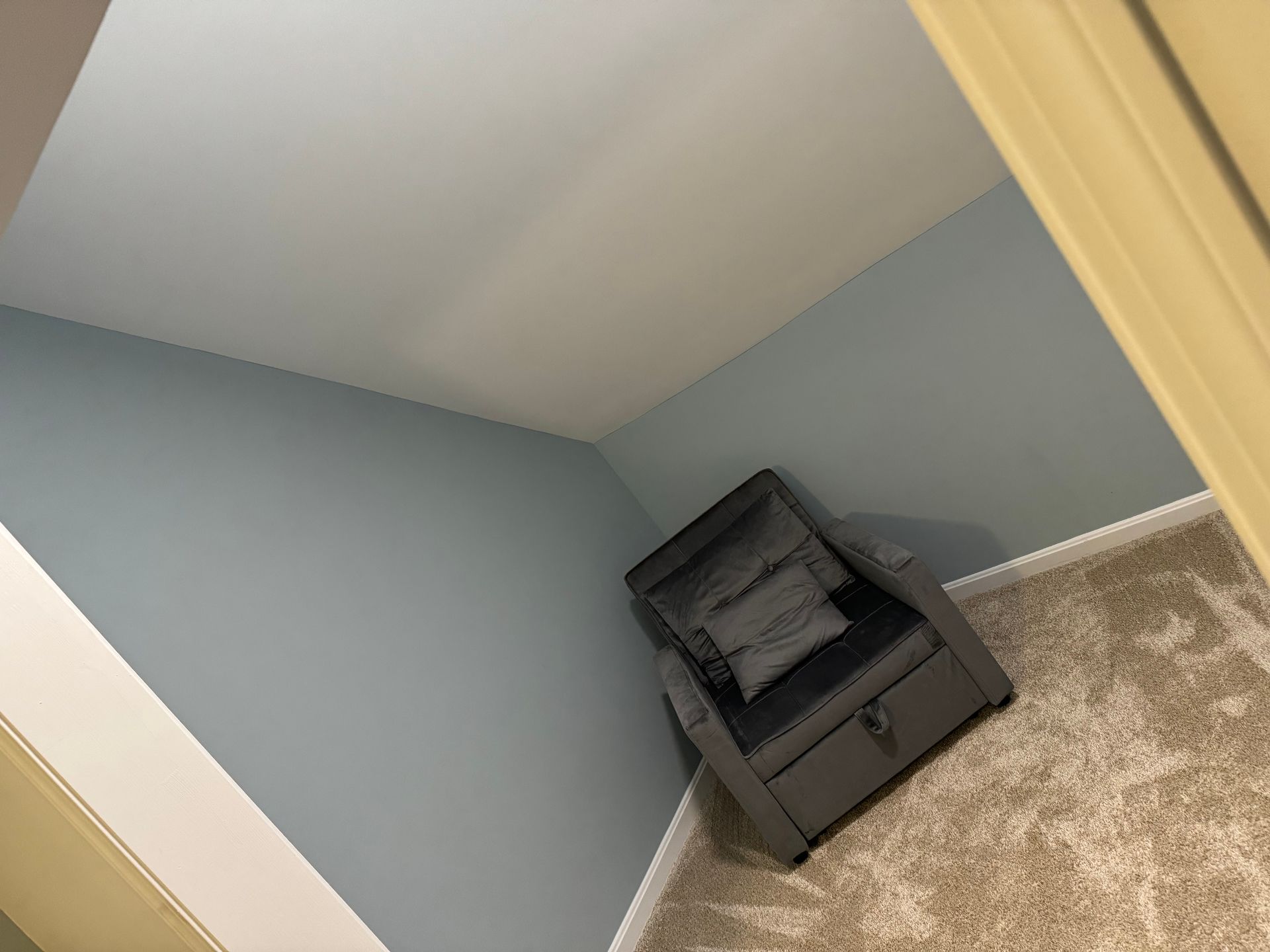Gray chair in a corner of a room with blue walls and tan carpet.