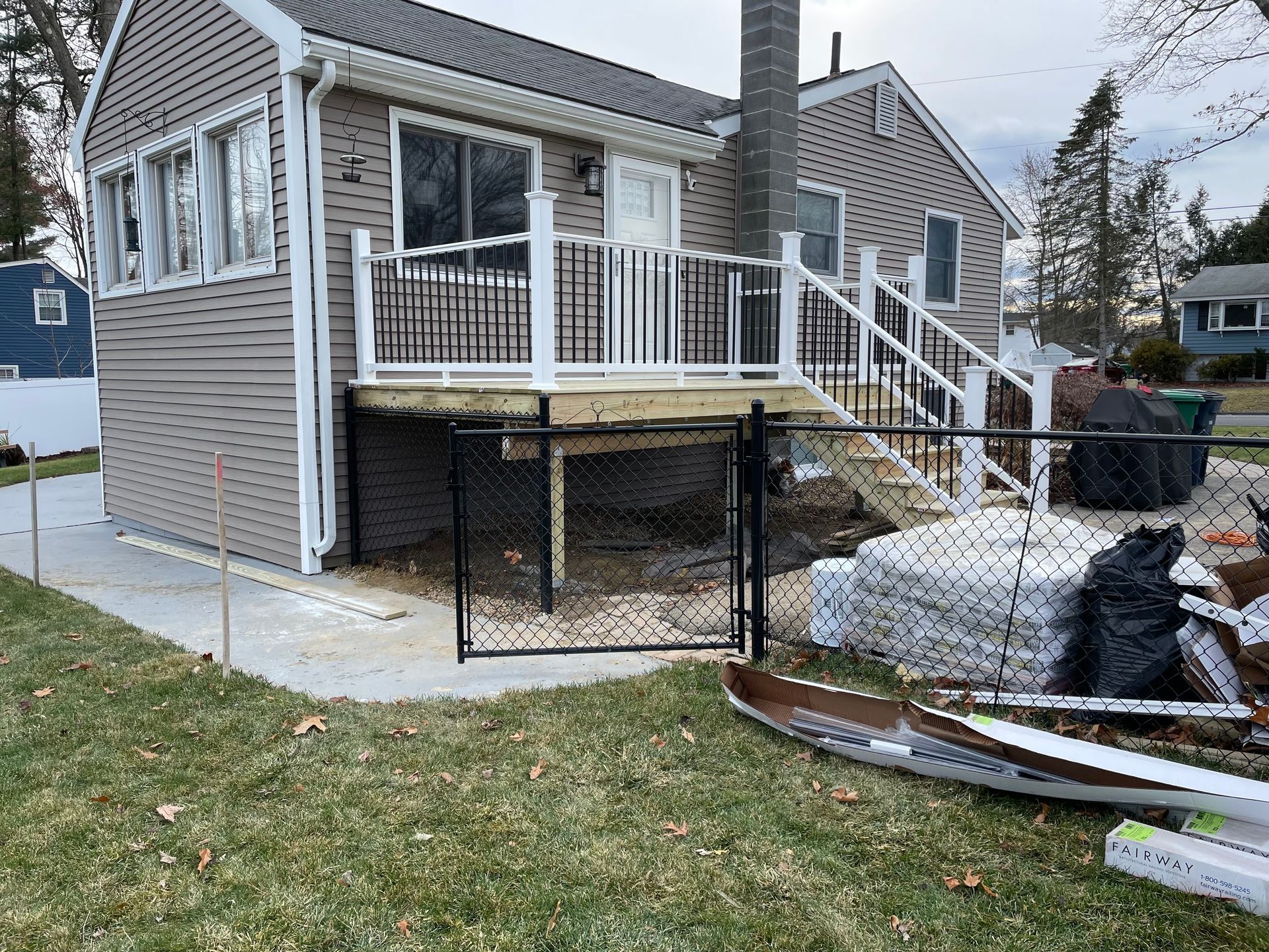 Tan house with deck and black fence in a yard with grass. Construction materials visible.