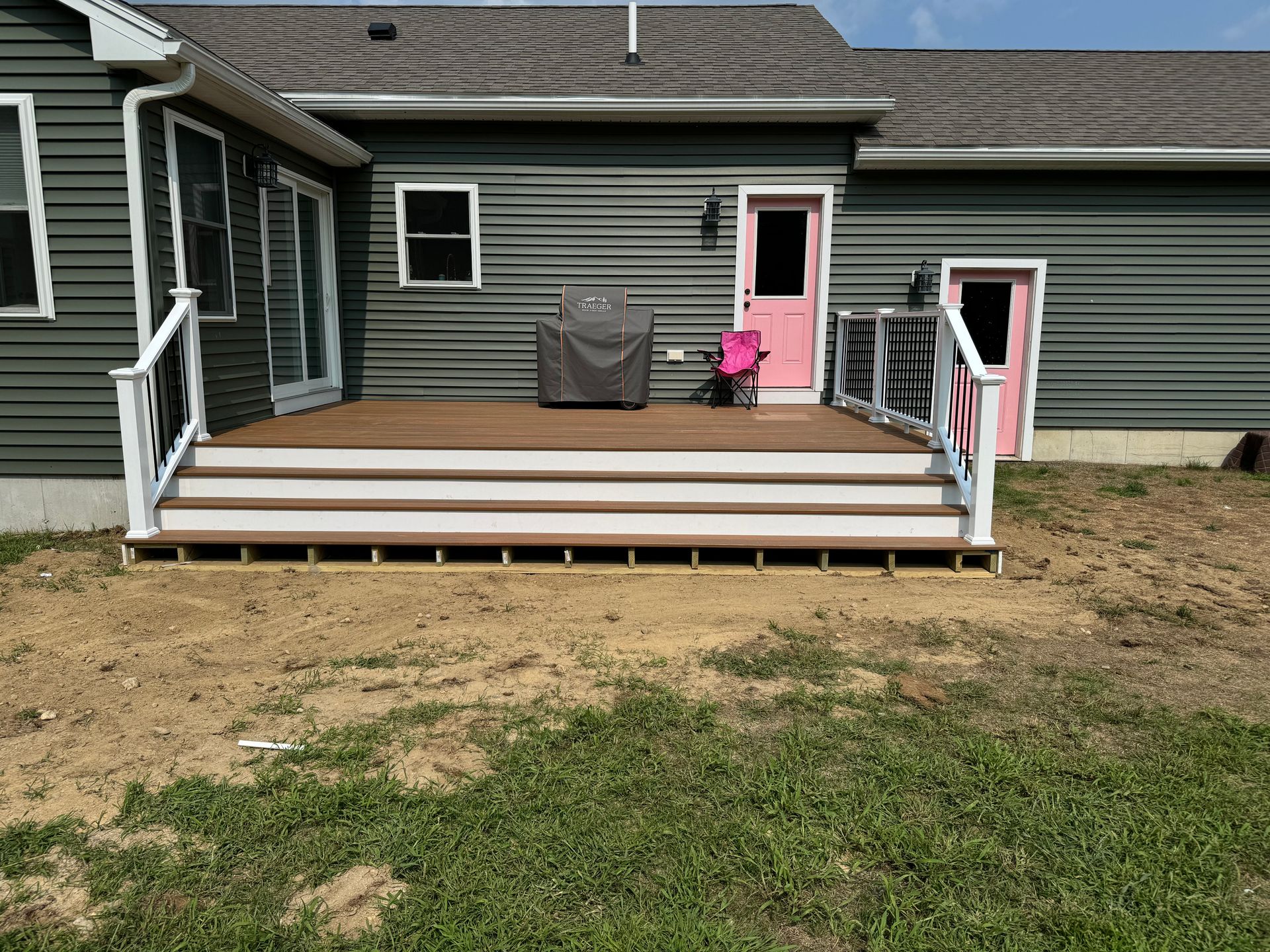 Deck with steps and railing attached to a green house with pink doors.