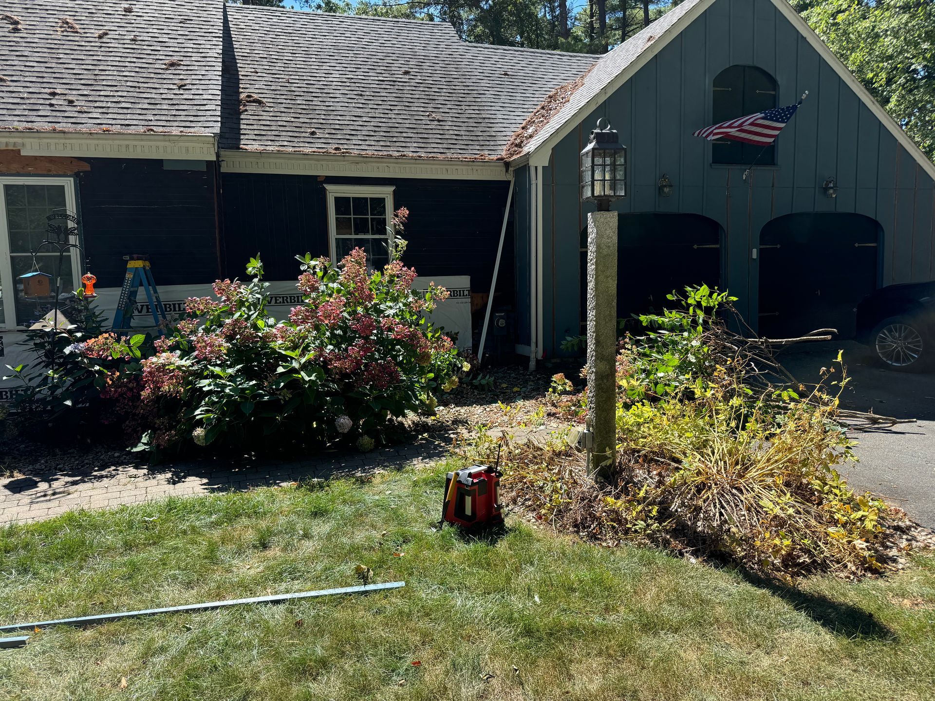 A dark blue house with a garage and a garden. A red object sits on the lawn.