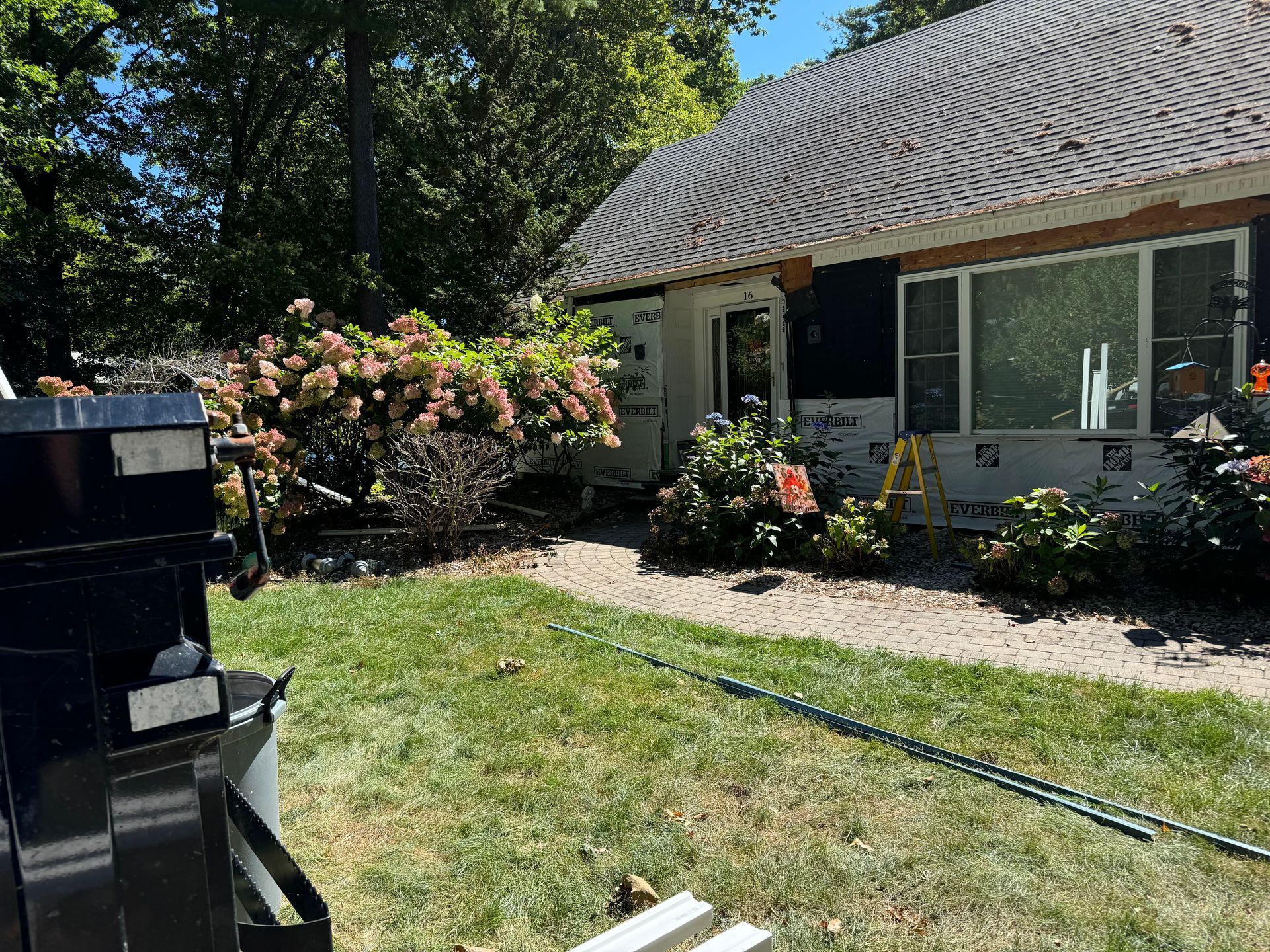 House exterior during renovation with exposed siding, surrounded by greenery, on a sunny day.