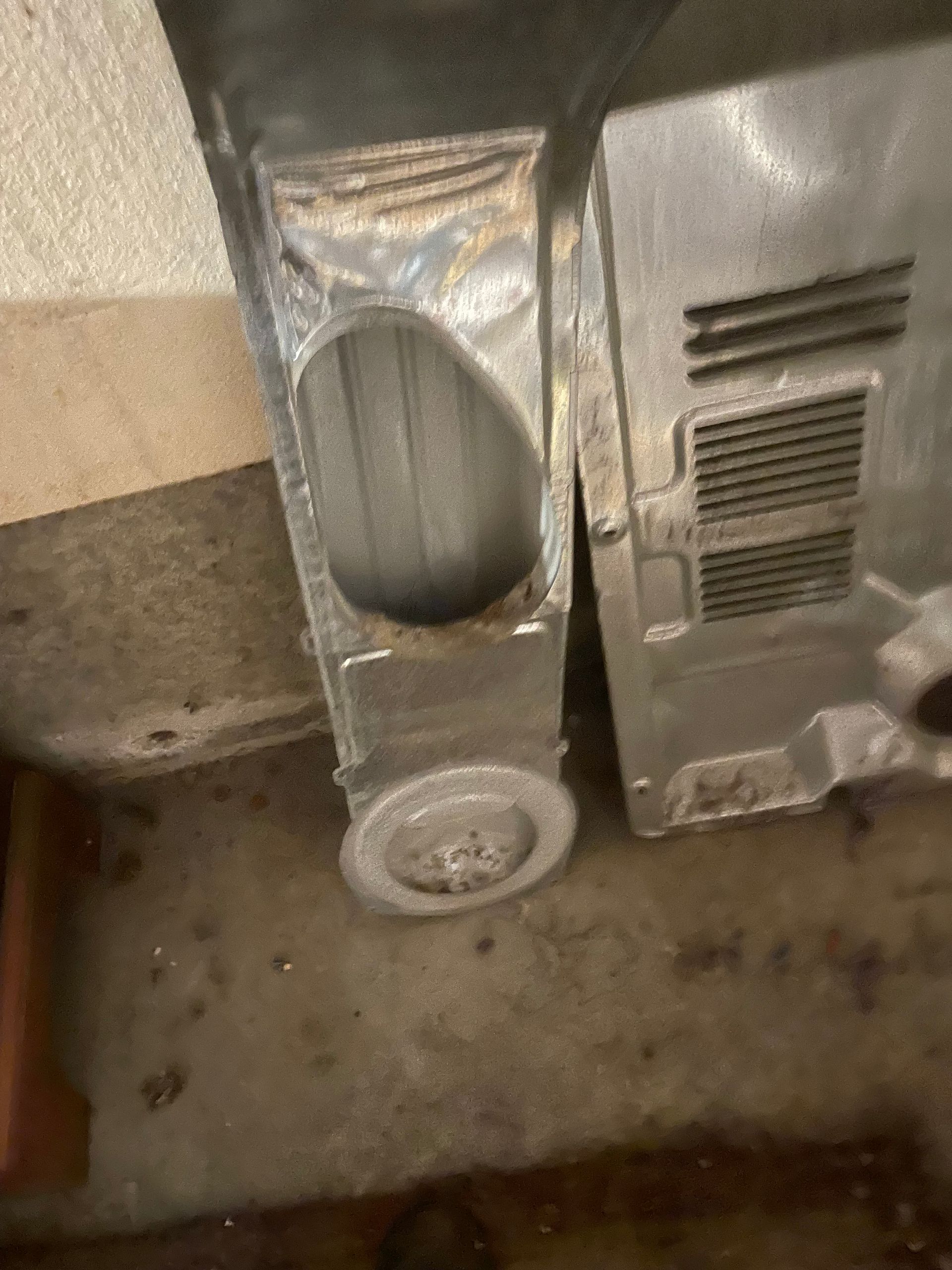 Metal appliance parts, showing a rectangular opening, and a wheel, resting on a dark surface.