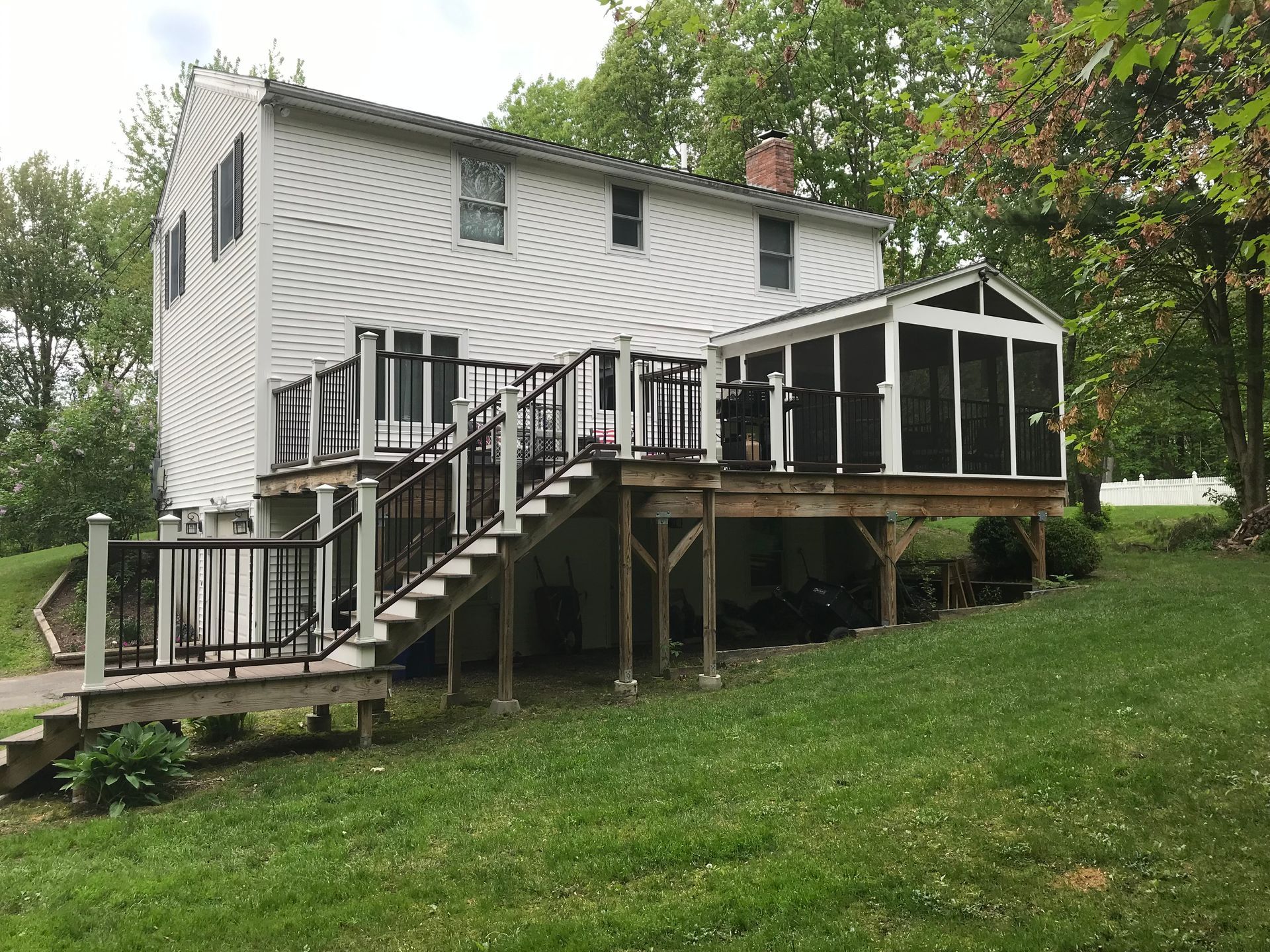 White house with deck and screened porch, on a grassy hillside.